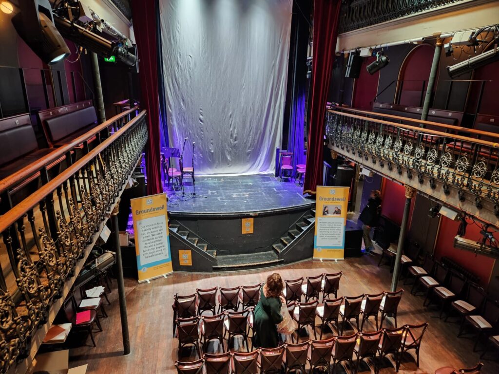 Image of a stage and hall with empty chairs waiting to be filled. Groundswell banners are on either side of the stage