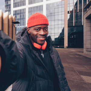 Testimonials FB (1) A man smiling at the camera in a dark coat and wearing an orange winter hat, somewhere in the street